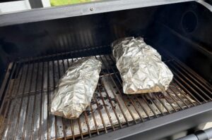Zwei in Alufolie eingewickelte Cadillac-Cut-Spare-Ribs auf dem Grillrost eines Gasgrillers während des Garprozesses