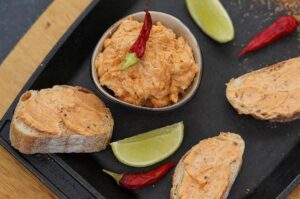 Cajun-Butter auf Toastscheiben verteilt, Schale mit Butter, Limettenspalten und rote Chilischoten auf schwarzem Servierbrett