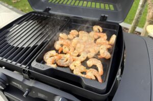 Garnelen mit Cajun-Gewürzen auf schwarzer Grillplatte im offenen Gasgrill braten