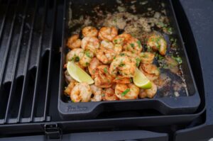 Cajun-Garnelen in schwarzer Grillpfanne auf dem Grill, gewürzt mit Petersilie, garniert mit Limettenspalten