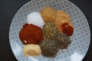 Cajun-Gewürzmischung auf grauem Teller: Paprika, Cayennepfeffer, brauner Zucker, Knoblauch- und Zwiebelpulver, getrocknete Kräuter, Salz und Gewürze