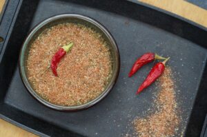 Selbstgemachtes Cajun-Gewürz in einer Schale mit getrockneten roten Chilischoten auf schwarzem Tablett