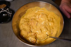 Goldgelbe Chicken-Tikka-Masala-Sauce mit cremiger Konsistenz in einer Metallschüssel, mit Hähnchenstücken durchmischt