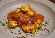 Chicken Tikka Masala mit würzigen Hühnchestücken auf Cremesauce und Reisbett, garniert mit grünen Kräutern und Chilischoten