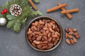 Gebrannte Mandeln in einer Schüssel mit Zimtstangen, Tannenzapfen, Beeren und Kugel als Weihnachtsdeko
