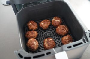 Acht braun gebratene Frikadellen in der Heißluftfritteuse auf dem Gitterrost während der Zubereitung