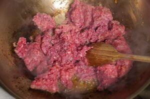 Rohes Rinderhackfleisch wird in einer Wok-Pfanne mit Holzlöffel gerührt und angebraten