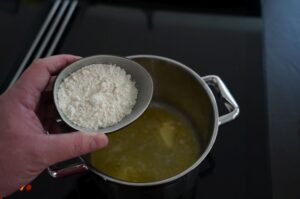 Hand hält eine Schöpfkelle mit Mehl über einen Topf mit goldgelber Butter zur Herstellung von Béchamelsauce