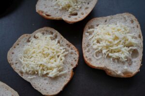 Aufgeschnittene Brötchen mit geriebenem Käse belegt, vorbereitet zum Grillen