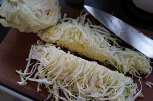Fein geschnittener Krautsalat auf Holzbrett, teilweise mit Messer portioniert