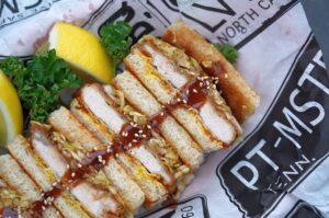 Katsu Sando mit paniertem Schnitzel, Sauce und Sesam zwischen Toastbrot, garniert mit Petersilie und Zitronenscheiben