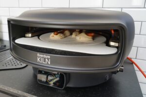 Everdure KILN Pizzaofen mit Pizza-Dogs: Würstchen in Pizzateig auf runder Steinplatte bei 405°C im Innenofen