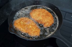 Zwei goldbraun frittierte Tonkatsu-Schnitzel mit knuspriger Panierung in siedendem Öl in der Grillpfanne