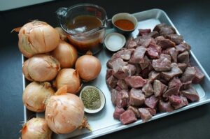 Zutaten für Wiener Saftgulasch: gewürfelte Rinderfleischstücke, ganze Zwiebeln, Rinderbrühe, Tomatenmark, Sour Cream und Majoran