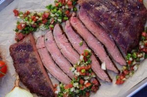 Gegrilltes Flanksteak in dünne Scheiben geschnitten, daneben gehäufte brasilianische Salsa aus Tomaten, Zwiebeln und Koriander