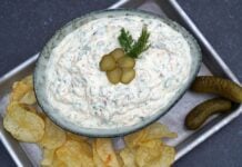 Pickle-Dip in Schale mit Dill-Garnierung und eingelegten Gurkenscheiben, serviert mit Kartoffelchips und Salzgurken