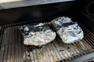 Zwei in Alufolie gewickelte Wildschwein-Ribs auf dem Grillrost beim Garen