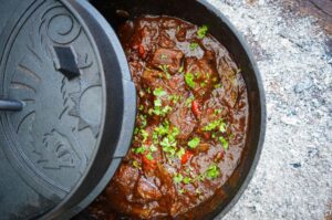 Brauhaus-Gulasch im Dutch Oven, Gulasch mit Soße und Fleischstücken, garniert mit Petersilie und Paprikastücken
