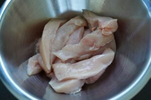 Rohe Hühnerbrustfilets in Streifen geschnitten in einer Edelstahlschüssel zur Vorbereitung von Chicken Fingers