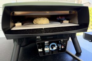 Döner-Bomb-Pizza im Pizzaofen auf kreisförmigem Stein, Flammen im Hintergrund, digitales Thermometer zeigt 318°C