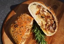 Aufgeschnittene Döner-Bomb mit Dönerfleisch, Käse und Zwiebeln im Sesambrötchen, garniert mit Rosmarin auf Holzbrett