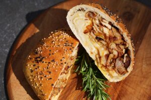 Aufgeschnittene Döner-Bomb mit Dönerfleisch, Käse und Zwiebeln im Sesambrötchen, garniert mit Rosmarin auf Holzbrett
