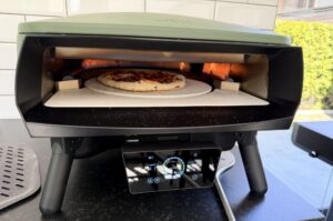 Pizza Peperoni mit Peperoni-Belag in Pizzaofen auf Schamottstein, Flammen sichtbar, während des Backens