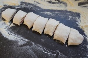 Sechs gefüllte Pizzabrötchen mit Schinken und Käse auf mehlbestäubter dunkler Arbeitsfläche, vor dem Backen.