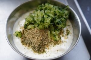 Schüssel mit Tzatziki-Sauce, frischen Gurkenstücken und Kräutern, oben mit Gewürzmischung bestreut