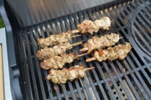 Gyros-Hähnchenspieße auf Holzspießen grillen auf schwarzem Grillrost, zeigen gebräunte Oberflächen und Gewürzkruste