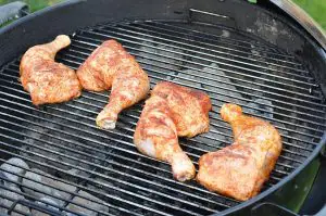 Gegrillte Hähnchenschenkel mit Raucharoma auf schwarzem Kugelgrill, goldbraun und knusprig gebräunt auf Grillrost