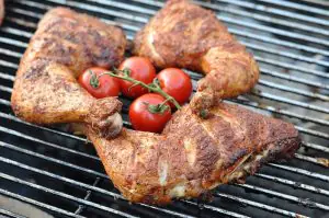 Gegrillte Hähnchenschenkel mit Röstkruste auf dem Grillrost, garniert mit frischen Tomaten am Rebstück