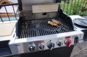 Kokos-Limetten-Hähnchenspieße 10 Kokos-Limetten-Hähnchenspieße auf Grillspießen auf dem Rost eines Gasgrill mit Gusseisenplatte, daneben leere Servierteller.