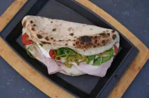Panuozzo mit Schinken, Mozzarella, Tomaten, grünem Pfeffer und Rucola auf schwarzem Tablett