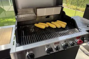 Fünf Maiskolben auf dem Grill eines Gasgrillers, Vorbereitung für Esquites, mexikanischer Maissalat