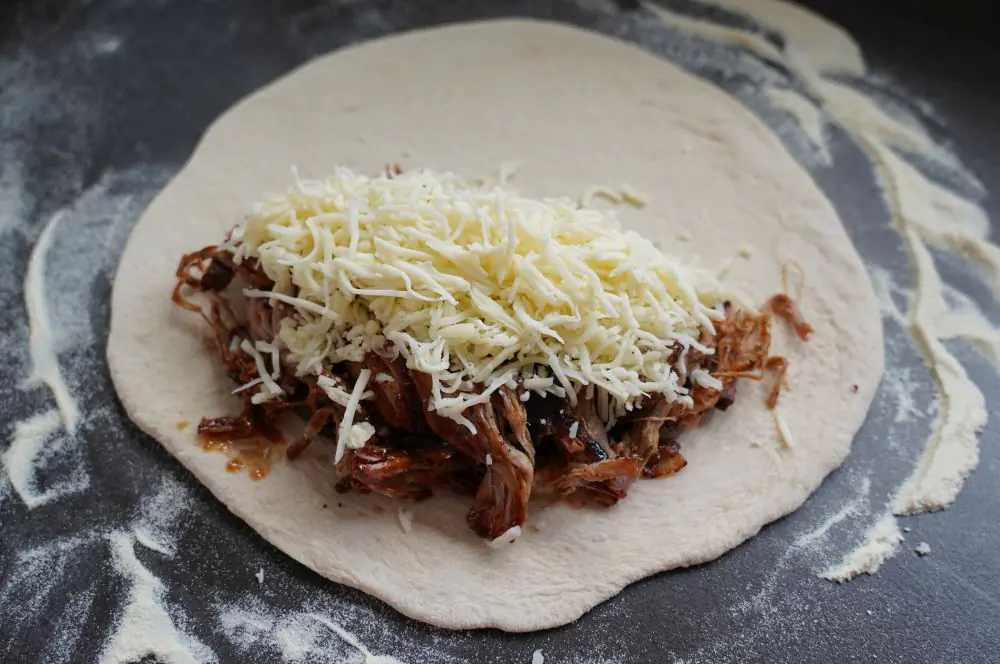 Der Pizzateig wird mit Pulled Pork und Käse belegt