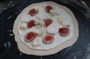 Flammkuchen mit Creme fraîche, halbierten frischen Feigen und Ziegenkäse auf schwarzem Grillblech