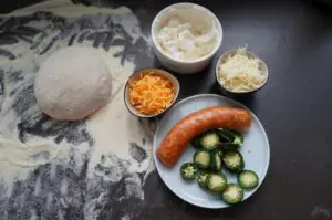 Pizzateig mit Mehl, Cheddar-Käse, geriebener Käse, geriebene Karotte, Jalapeño-Scheiben und Donlicate Cheddar Chili Brat für Jalapeño Popper Pizza