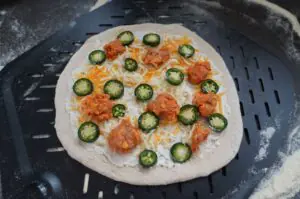 Ungebackene Jalapeño-Popper-Pizza auf Grillplatte mit Cheddar, gegrillten Brat-Stücken und frischen Jalapeño-Scheiben