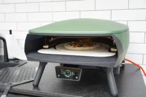 Jalapeno-Popper-Pizza mit Toppings in grünem elektrischen Pizzaofen, Temperaturanzeige zeigt 364°C, weiße Fliesenwand im Hintergrund