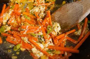 Pad Thai mit Garnelen auf dunkler Grillplatte, umgerührt mit Holzspatel, Garnelen mit Erdnüssen, grünen Zwiebeln und Chili