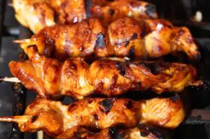 Yakitori-Spieße mit mariniertem Hähnchenfleisch auf dem Grill, goldbraun und mit Grillmarks gebräunt, auf Metallspießen