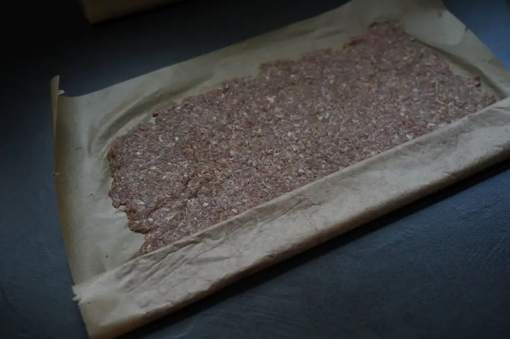 Das Hackfleisch wird mit dem Backpapier aufgerollt