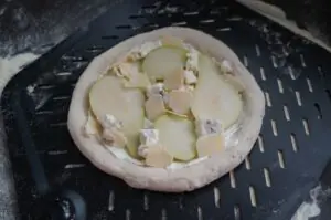Pizza mit Birnenscheiben, Gorgonzola und Walnüssen auf schwarzem Grillstein vor dem Grillen