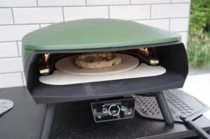 Flammkuchen mit Birne, Gorgonzola und Walnüssen auf dem Pizzastein eines grünen Elektrogrills mit Temperaturregler