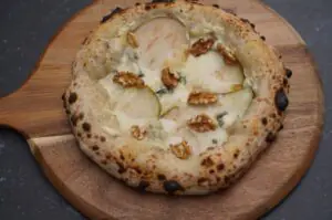 Pizza Birne Gorgonzola mit Walnusskernen auf Holzbrett, geflammter Teigrand mit Brandflecken, Birnenslices und Walnusshälften auf cremiger Käsesauce