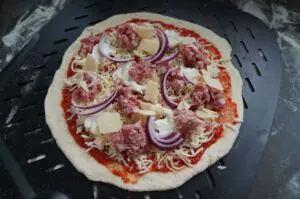Salsiccia-Pizza auf Grillplatte: Teig mit Tomatensoße, italienischer Wurstbrät, Ziegenkäse und roten Zwiebelnringen