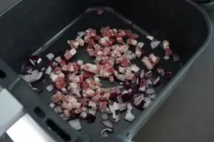 Gewürfelte Speckstücke und Zwiebelwürfel in schwarzem Grillbehälter