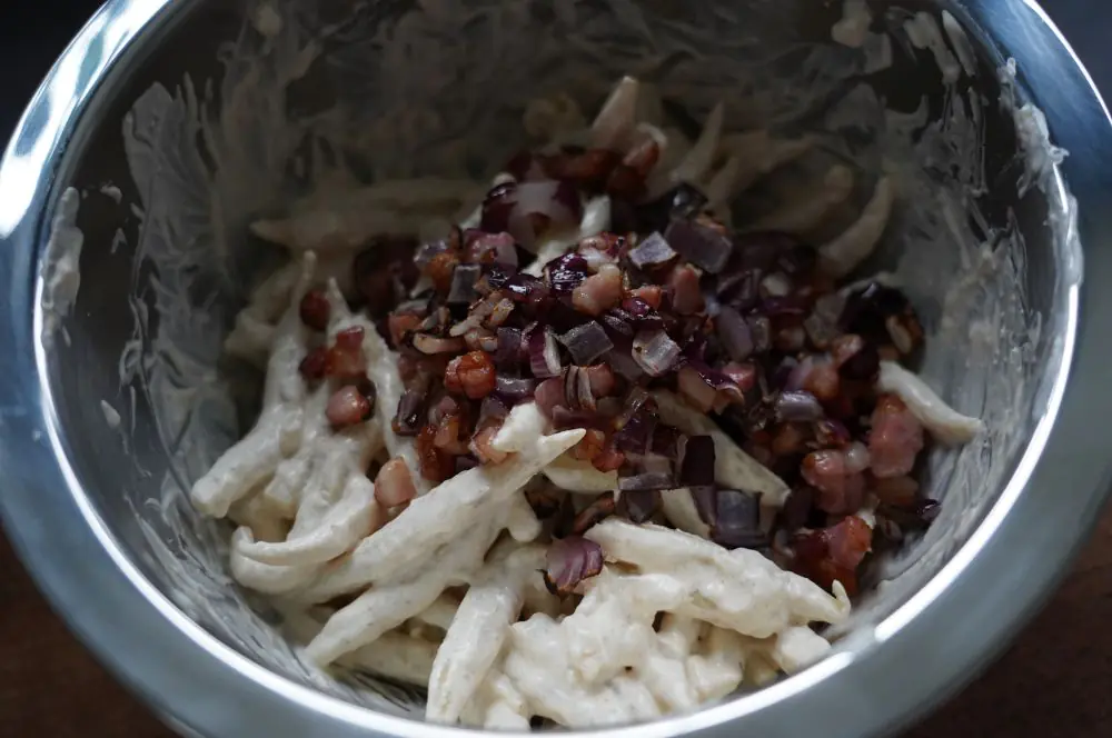 Die Schupfnudeln werden mit der Sauce, Speck und Zwiebeln vermengt