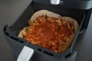 Schupfnudeln-Flammkuchen in der Heißluftfritteuse goldbraun ausgebacken, auf Backpapier in schwarzem Frittierkorb
